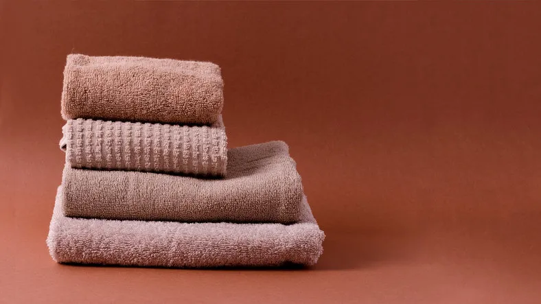 a stack of clean brown cotton towels on a brown background with a copy of the space
