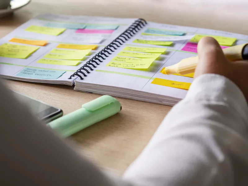 close-up of agenda organize with color-coding sticky notes for time management productive schedule for appointments and reminders hand holding a yellow highlighter marker organization and planning