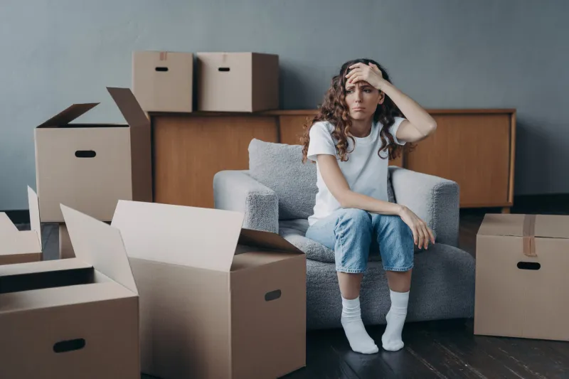headache from moving exhausted woman sitting among packed cardboard boxes spanish young lady in jeans and white t-shirt going to relocate depression and stress from moving concept