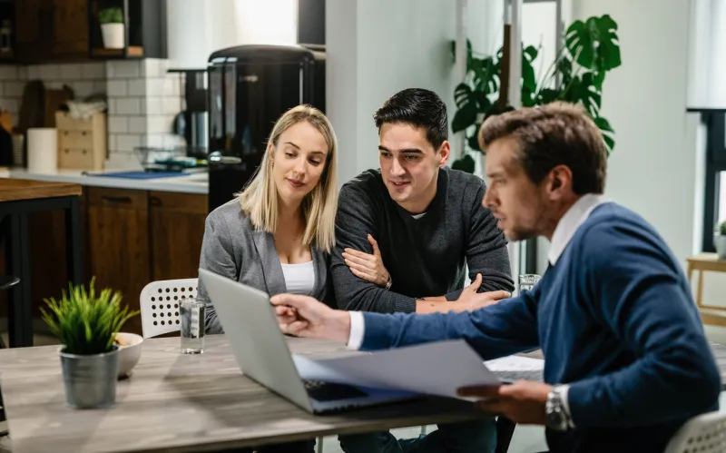 young couple and real estate agent using laptop while going through housing plan on a meeting
