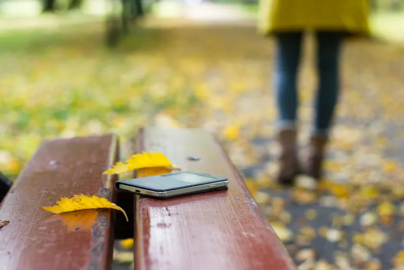 forgotten smart phone on a park bench woman is leaving from a bench where she lost her cell phone