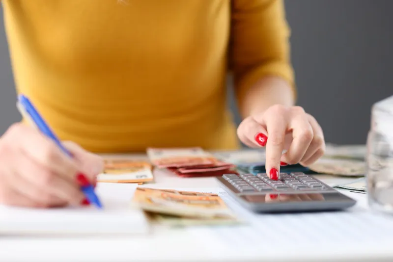 woman is counting on calculator and writing with pen in notebook closeup home budget concept