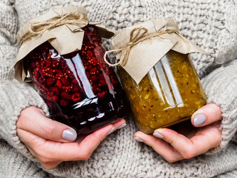two glass jars with jam in the hands of girls a girl in a wool sweater holding jars of jam cozy atmosphere