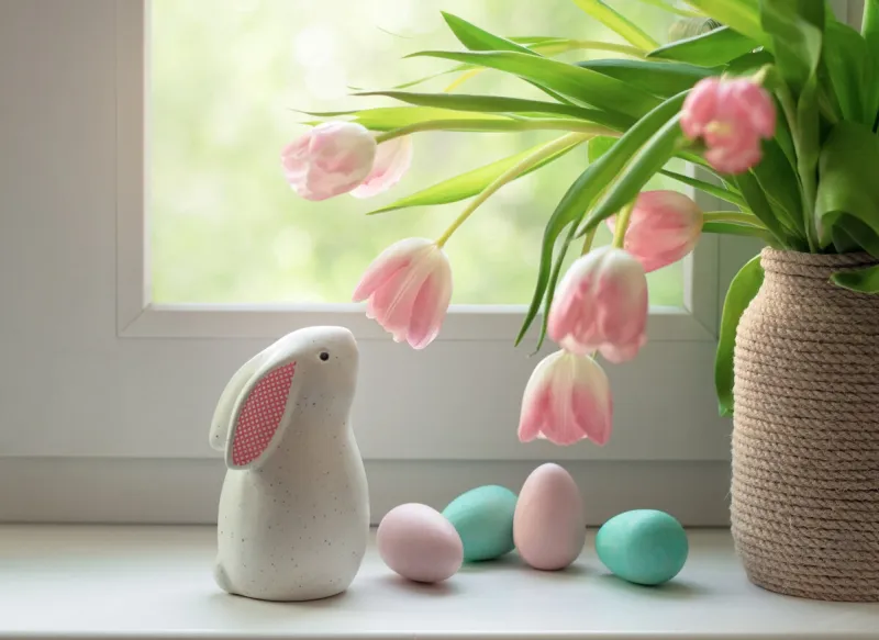 ceramic easter bunny, colorful dyed eggs and tulip flowers on windowsill decorations for easter celebration at home