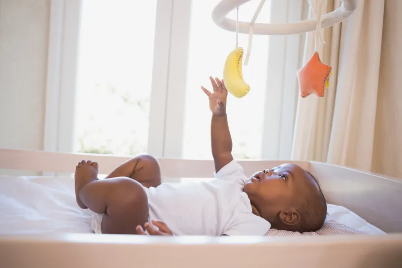 adorable baby boy lying in his crib playing with mobile at home in the bedroom