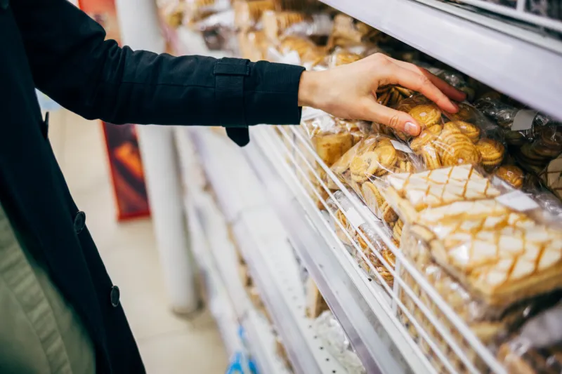 young woman choosing cookies near shelf in bakery department of grocery store, close-up