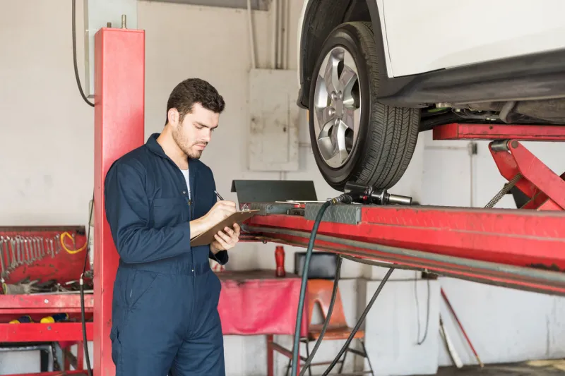 auto technician making checklist while standing by car in garage
