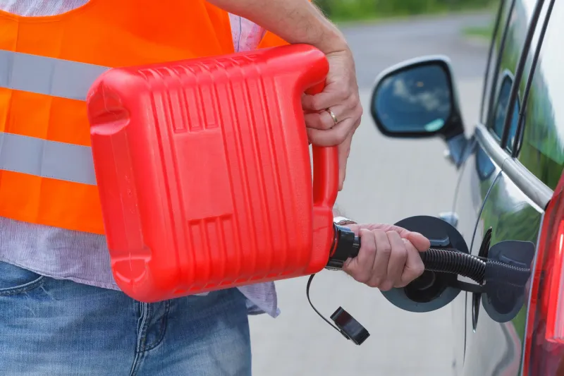 driver fills the fuel in an empty car tank from red canister on the side of the road