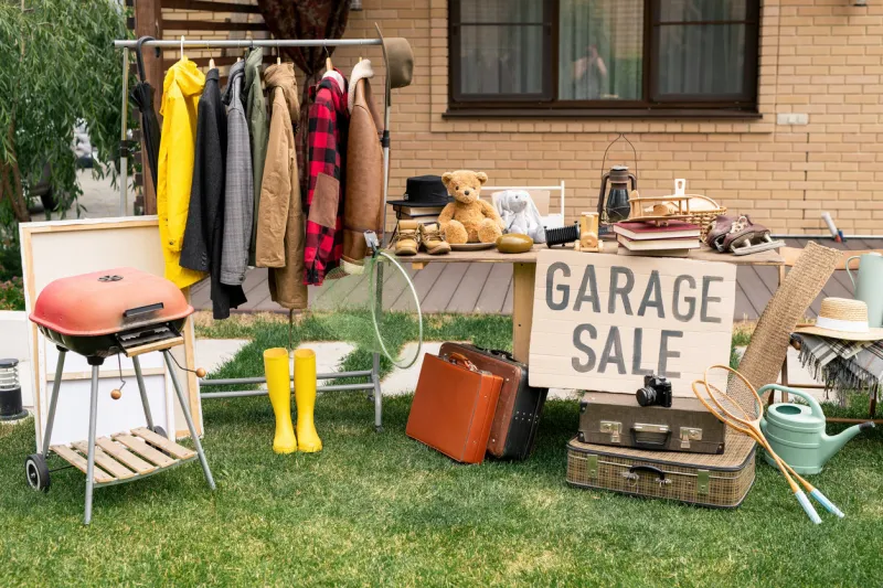 clothes rack, old-fashioned suitcases, garden tools and interior goods selling at garage market in backyard