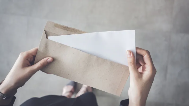 stand up woman holding white folded a4 paper and brown envelope