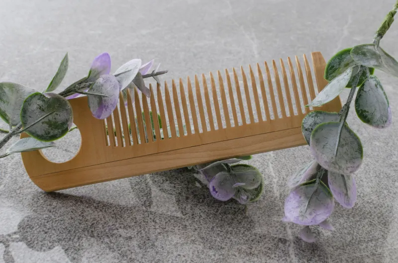 top view of wooden comb for hair and green leaves of eucalyptus on the grey bath surfaceempty space