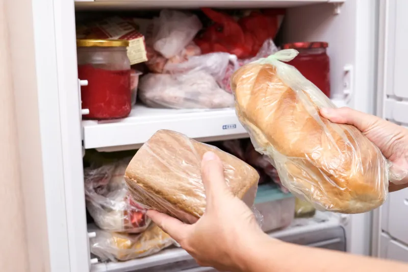 a hand putting two loafs of wheat and brown bread in reserve on a shelf of a home freezer, long life food storage concept