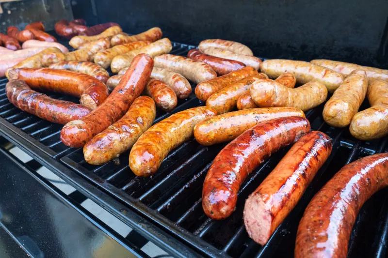 fresh sausage and hot dogs grilling outdoors on a gas barbeque grill