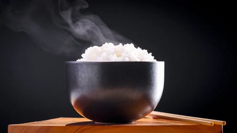 japanese rice, cook rice close up natural steaming cooked japanese white rice in black bowl with chopstick on black background, soft focus healthy food concept