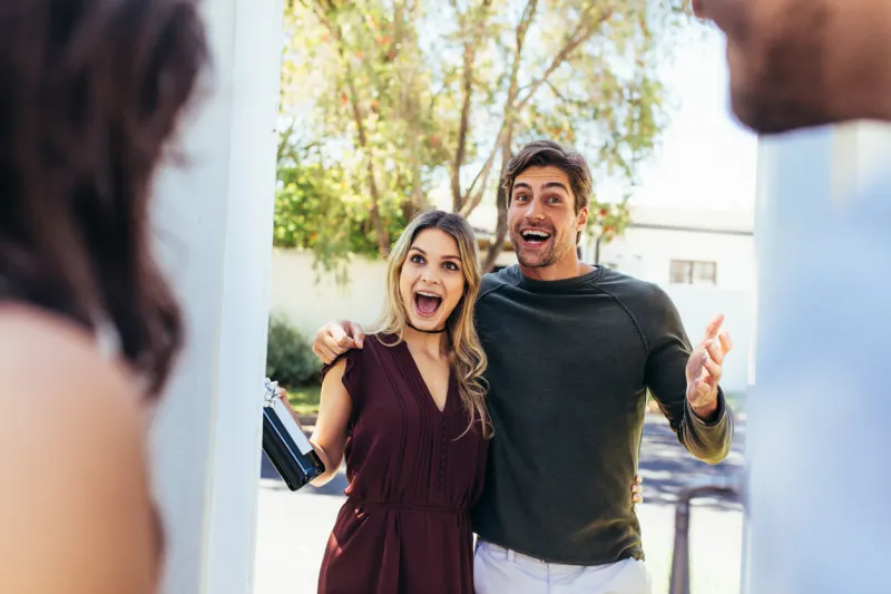 excited couple at entrance door with bottle of wine friends being welcomed by couple at the door attending friend's housewarming party