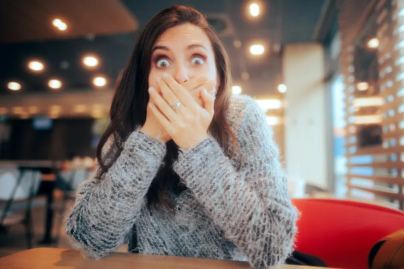 shocked woman covering her mouth sitting in a restaurant