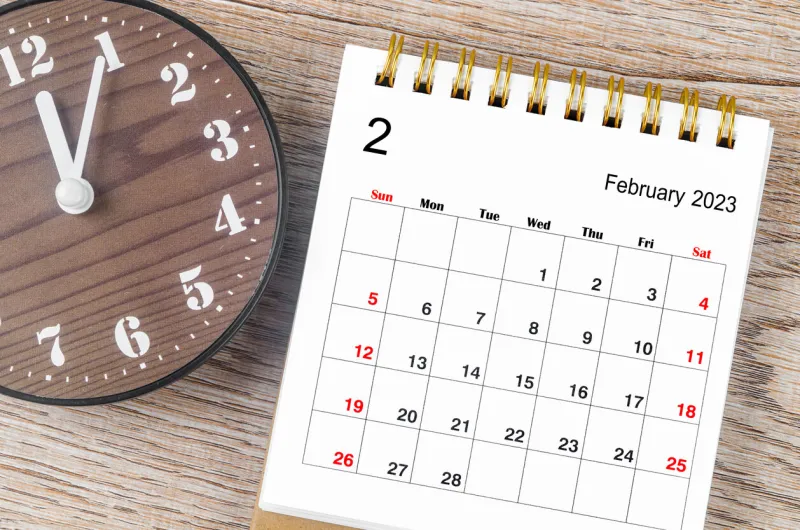 the february 2023 monthly desk calendar for 2023 year with wooden clock