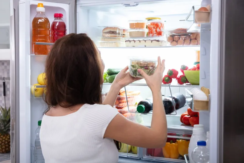 rear view of a young woman taking food from refrigerator