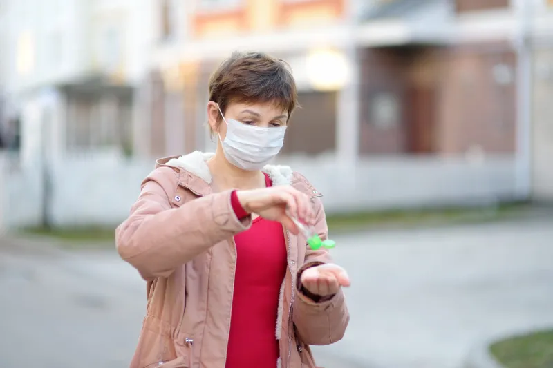 mature woman wearing medical face mask makes disinfection of hands with sanitizer on city streets or public place safety during covid-19 outbreak elderly people are risk group for coronavirus