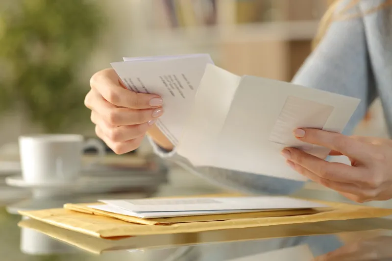 close up of girl hands opening an envelope with a letter inside on a desk at home