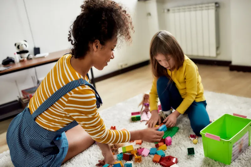 caucasian cute little girl spending time with african american baby sitter they are playing with construction toys set, sitting on the floor children education, babysitting concept selective focus