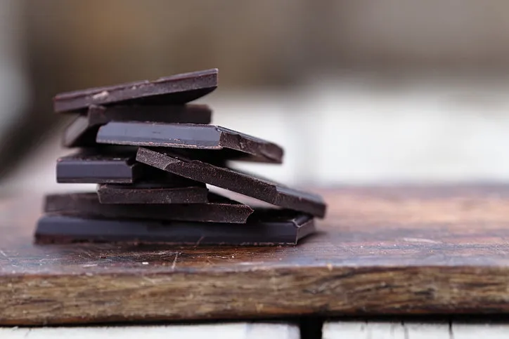 stack of broken dark chocolate bar pieces on a wooden background horizontal
