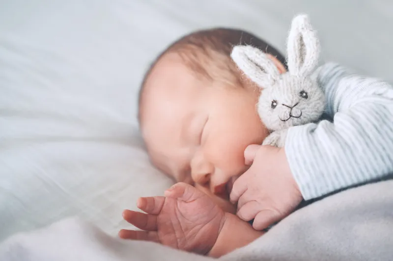 newborn baby sleep at first days of life portrait of new born child boy one week old sleeping peacefully with a cute soft toy in crib in cloth background