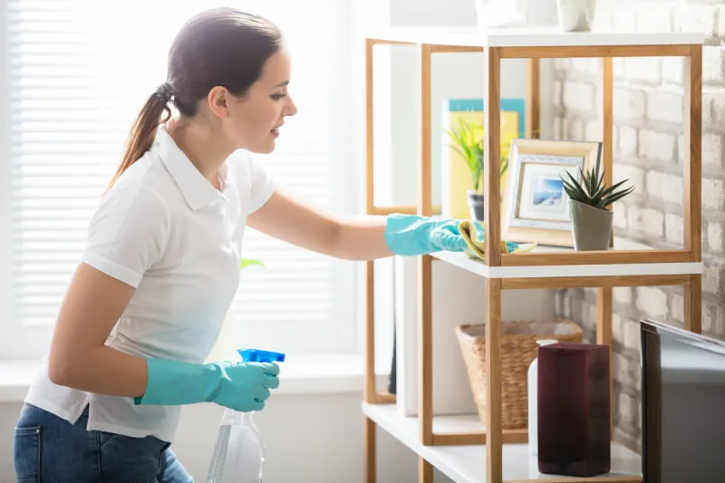 young woman cleaning the wooden shelf in living room
