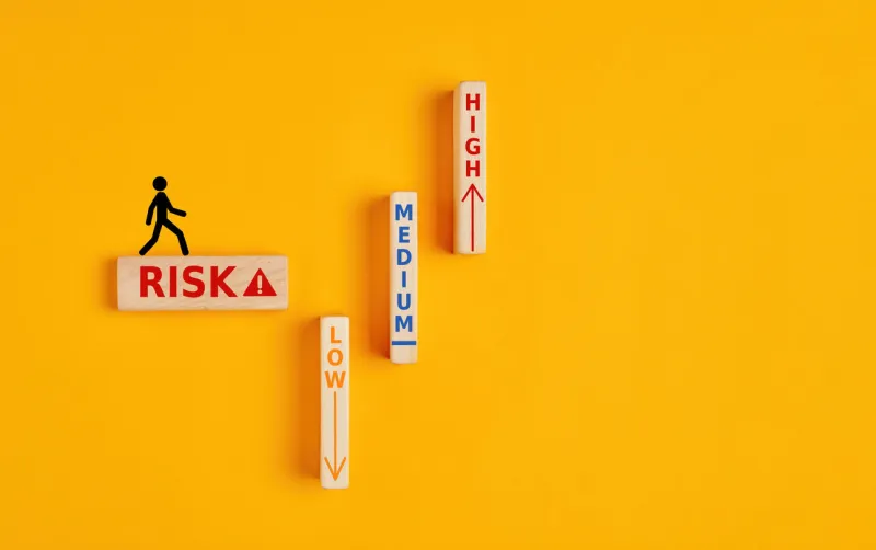 the words risk, medium, high and low written on wooden blocks with a stickman walking towrads the risk zone risk assesment, analysis or risk taking concept