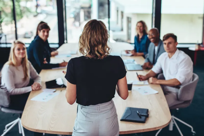 rear view of a businesswoman addressing a meeting in office female manager having a meeting with her team in office boardroom