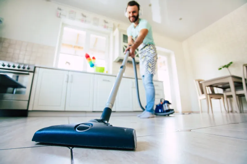 happy handsome young beard man is cleaning the floor in the domestic kitchen and have fun