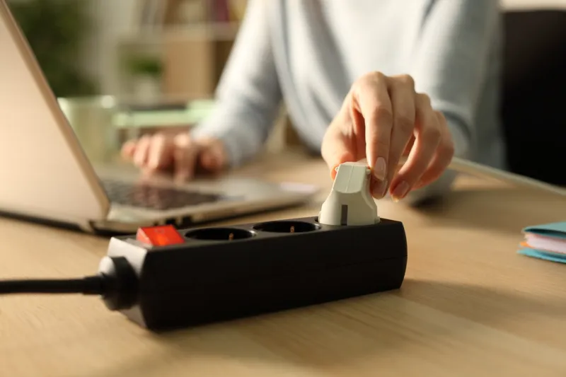 woman hand plugging plug on socket at night using laptop