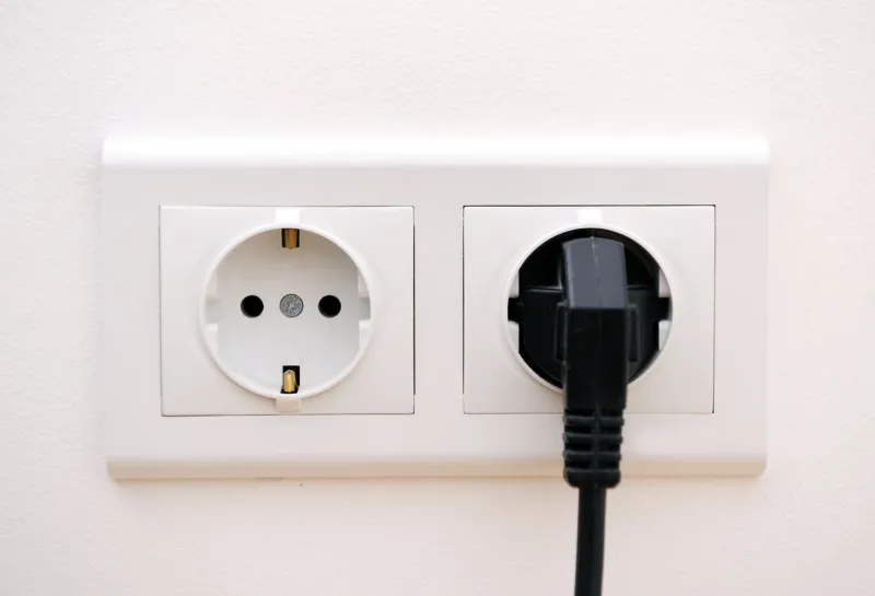 black electric chord plugged into a white electricity socket on white background