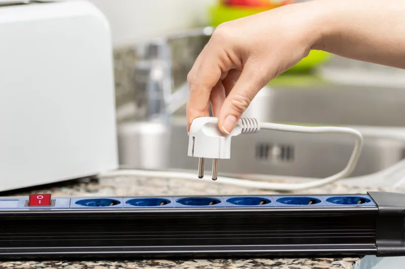 close up of a woman's hand plugging a toaster into the electrical outlet in a socket on a kitchen counter at home