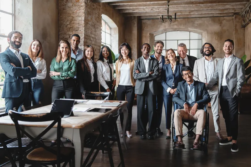 corporate portrait of a multigenerational working team with multiracial and disabled members - group photo of colleagues standing in the office in co-working space - business lifestyle concept