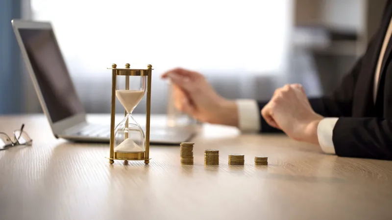 view on stack of coins and hourglass, business woman working on laptop in office
