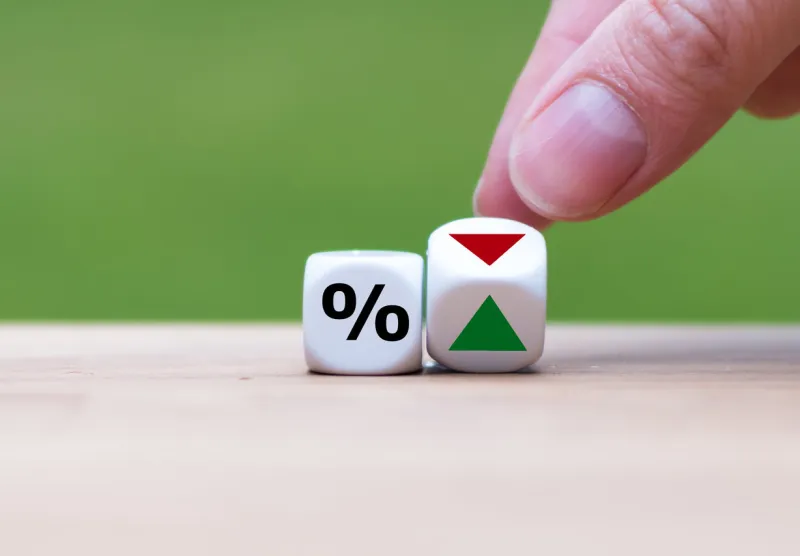 hand is turning a dice and changes the direction of an arrow symbolizing that the interest rates are going down (or vice versa)