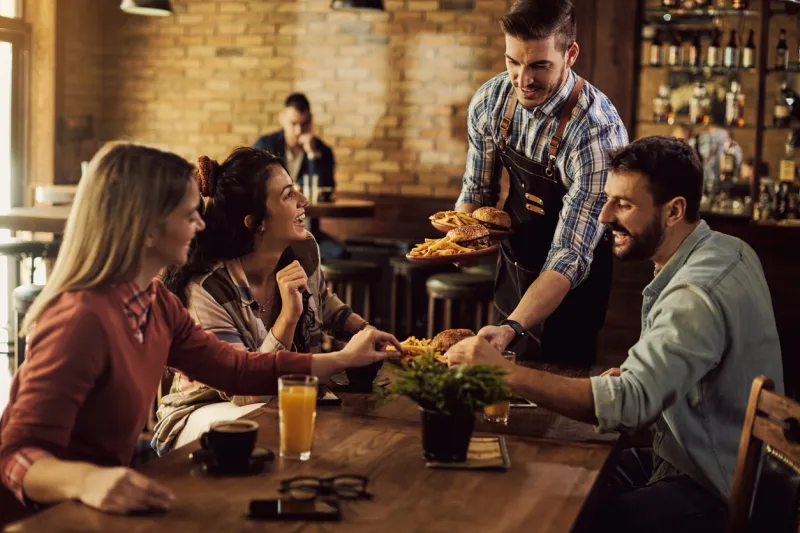 group of happy friends having fun while waiter is serving them food in a pub