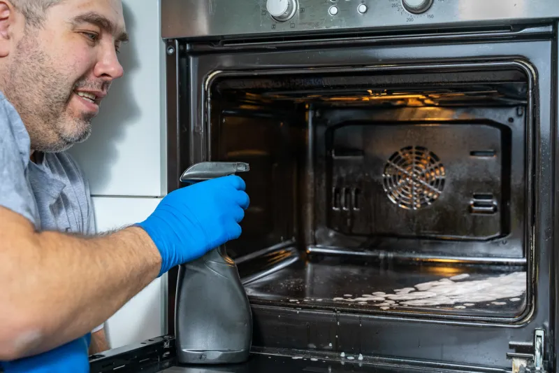 a man cleans the oven in his kitchen with a cleaning agent