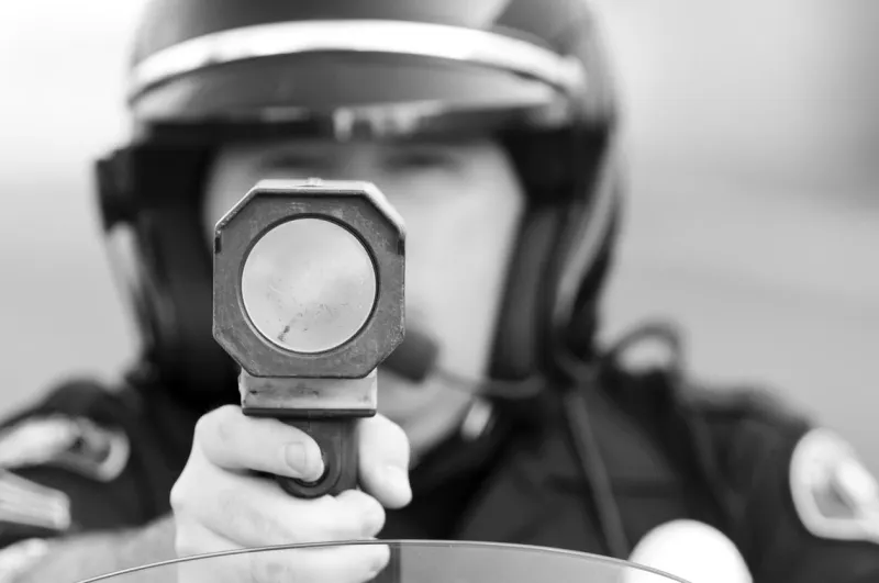 a motorcycle police officer holds his radar gun up at traffic