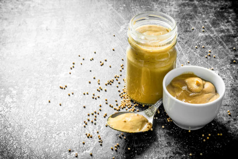mustard in a glass jar, spoon and bowl on dark rustic background