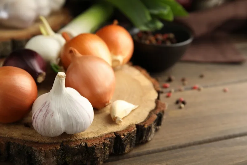 fresh onion bulbs, leek and garlic on wooden table, closeup space for text