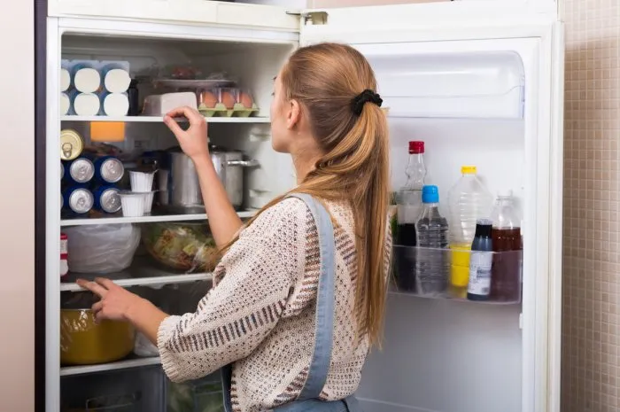 young housewife arranging products on fridge shelves