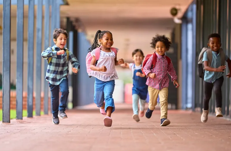 group of multi-cultural elementary school pupils running along walkway outdoors at school