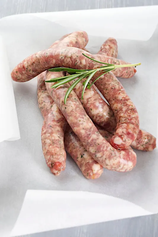 raw sausages chipolata with herbs in baking paper