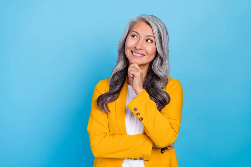photo of shiny dreamy senior lady dressed yellow blazer arm chin looking empty space smiling isolated blue color background