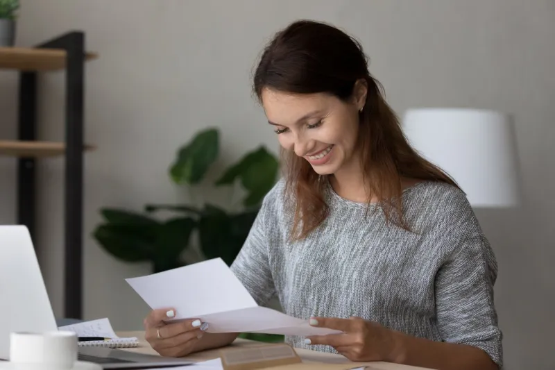 happy millennial woman reading paper correspondence letter, feeling excited by good news, getting last mortgage payment notification or invitation for event, sitting at home office workplace