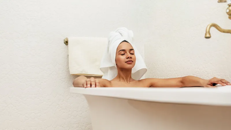woman with white towel on her head relaxing in bath with eyes closed