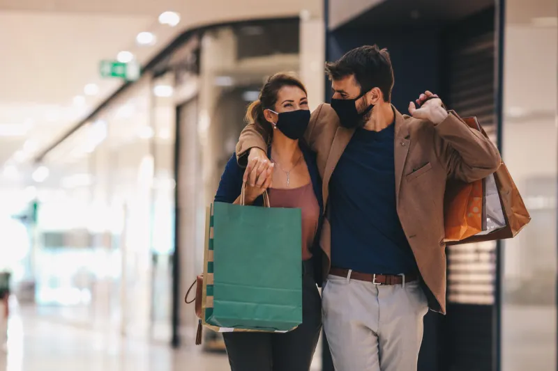 the young couple carries shopping bags and walks through the mall, wearing protective masks, life in a time of pandemic