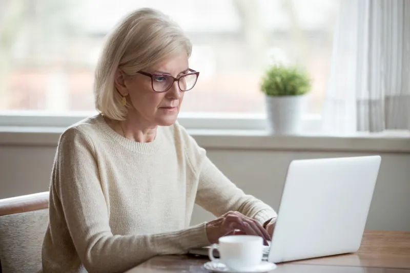 serious mature middle aged business woman in glasses using laptop typing email working at home office, thoughtful focused senior old lady searching information on internet or communicating online
